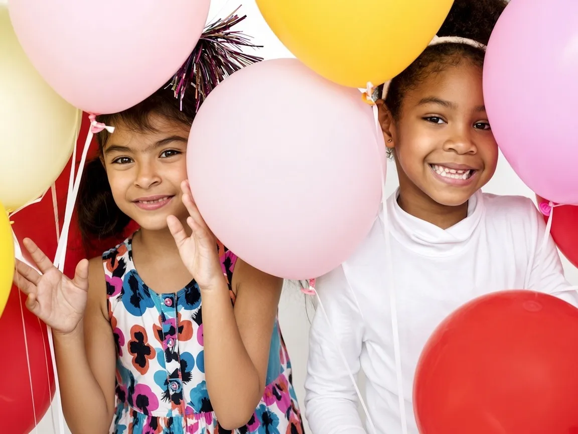 Two girls smiling among pink and gold balloons