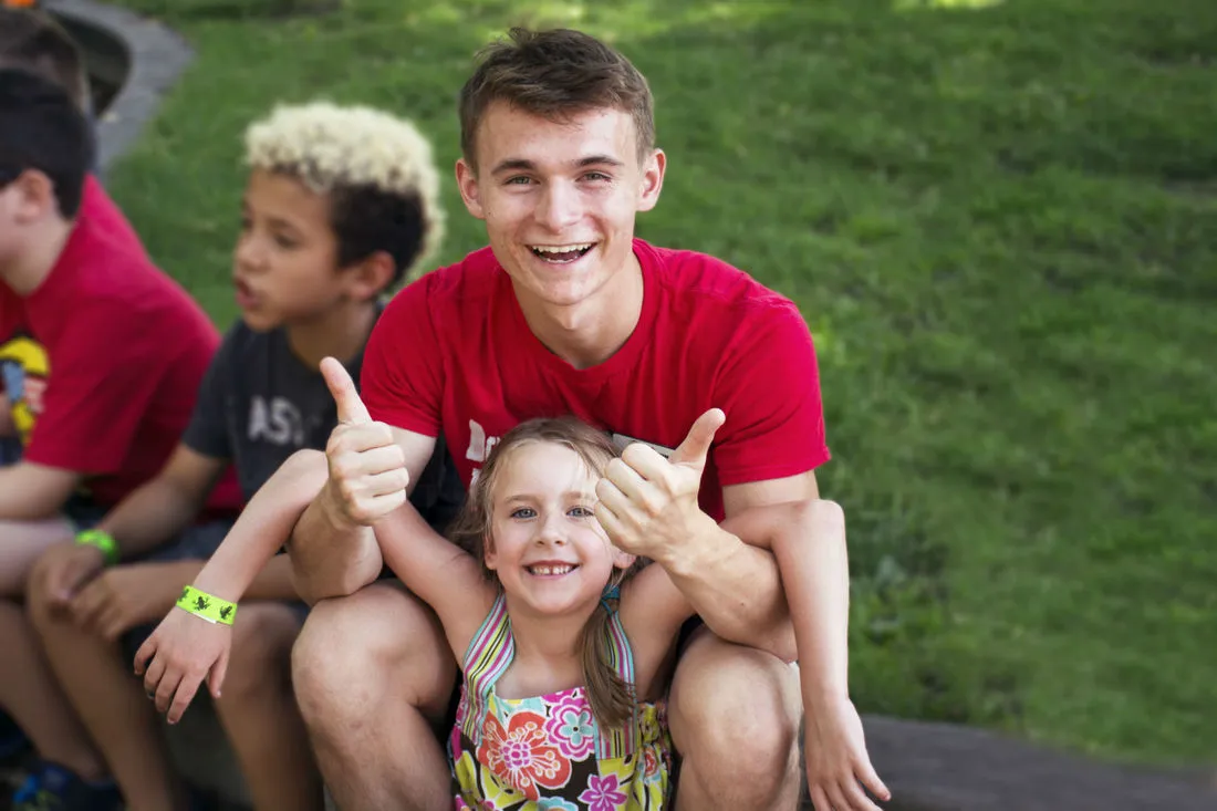 A camp counselor and kids giving thumbs up outdoors