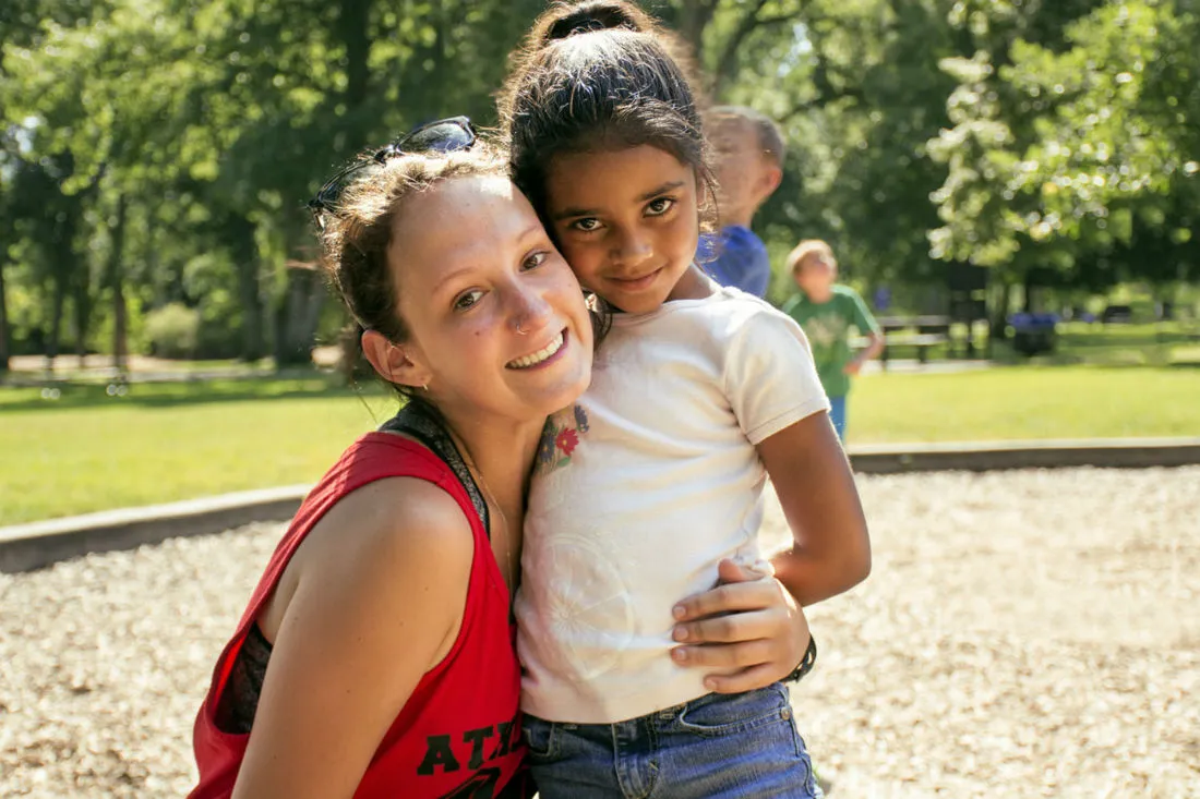 A counselor in a red shirt smiling with a camper outdoors