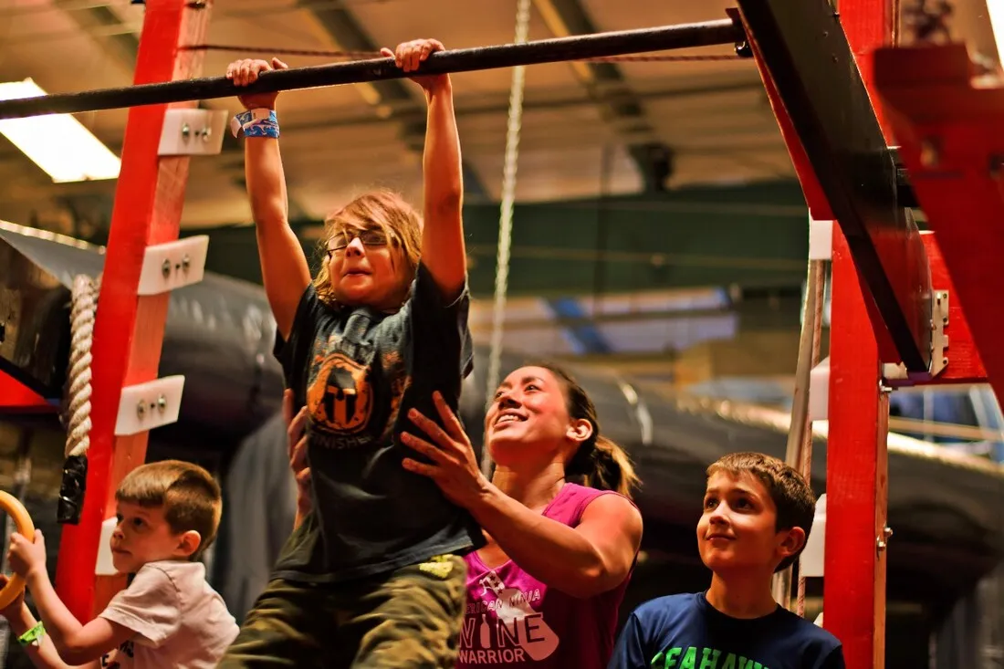 Campers cheering on a friend hanging from a ninja warrior bar